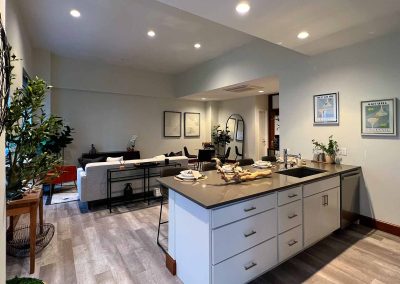 Modern kitchen with a central island, sleek cabinets, and a dining area in the background, complemented by decorative plant and wall art.