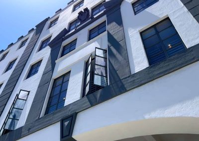 Low-angle view of a modern building's facade featuring curved and angular architectural elements, painted predominantly white and black, against a clear blue sky.