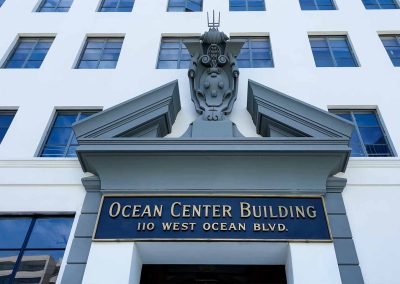 Facade of the ocean center building on 110 west ocean blvd, featuring a unique art deco design element above the entrance, against a clear sky.