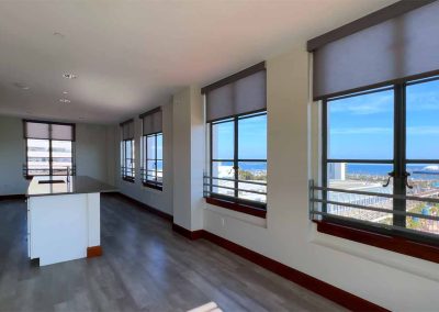 An empty, sunlit kitchen and living area featuring modern appliances, a central island, and large windows with a view of the ocean and coastal town.